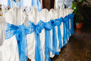 Beautiful white chairs with blue bows in restaurant. Wedding party setting with white draperies