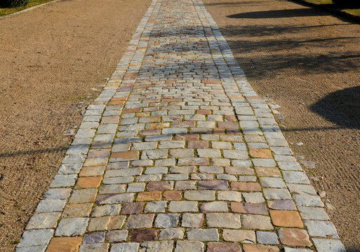 cobbled strip of beige brown cobblestone stones. around is a park gravel road of the castle's honorary courtyard. Centrally symmetrical division with lawns and spheres cut into old boxwoods