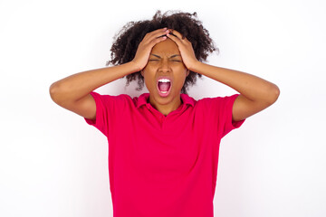 Shocked panic young beautiful African American woman wearing pink t-shirt against white wall holding hands on head and screaming in despair and frustration.