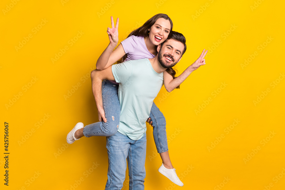 Poster Portrait of attractive funny cheerful couple guy carrying girl showing v-sign isolated over bright yellow color background