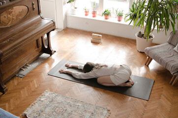 One beautiful young woman is doing yoga on an exercise mat in her living room. The room and her clothes are in vintage, retro style.