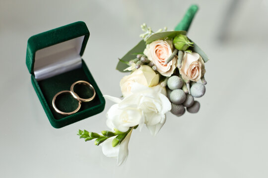delicate boutonniere with little roses and brunei and wedding rings on a glass surface