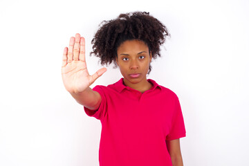 young beautiful African American woman wearing pink t-shirt against white wall doing stop gesture with palm of the hand. Warning expression with negative and serious gesture on the face.