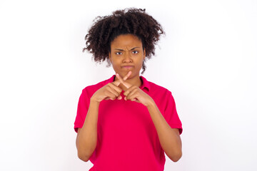 young beautiful African American woman wearing pink t-shirt against white wall has rejection angry...