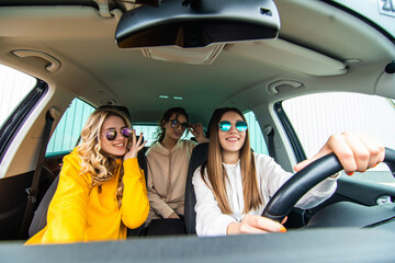 Three female friends in sunglasses enjoying traveling in the car.