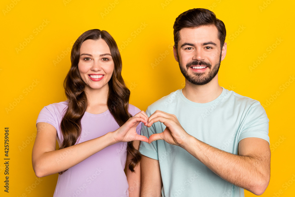 Poster Portrait of attractive amorous cheerful couple showing heart sign amour isolated over bright yellow color background