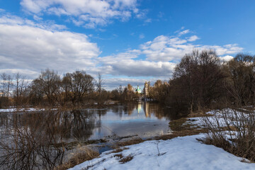 Spring flood. High water. Church on the banks of the river. Rural landscape in early spring. Clouds and trees reflected in the water.