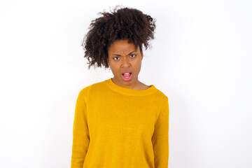 Obraz na płótnie Canvas Portrait of dissatisfied young beautiful African American woman wearing yellow sweater smirks face, purses lips and looks with annoyance at camera, discontent hearing something unpleasant