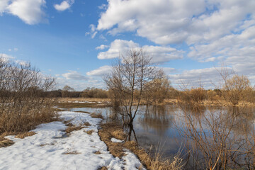 Spring flood, the river overflowed its banks. High water level in the river. Rural landscape in early spring. Clouds and trees are reflected in the water.