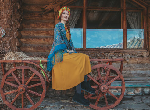 Russian beauty in traditional dress sits on a cart with hay 