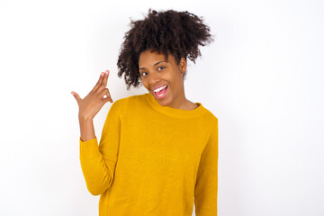 young beautiful African American woman wearing yellow sweater against white wall foolishes around shoots in temple with fingers makes suicide gesture. Funny model makes finger gun pistol