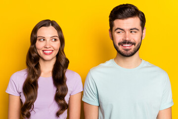 Portrait of attractive shy curious cheerful couple looking at each other isolated over bright yellow color background