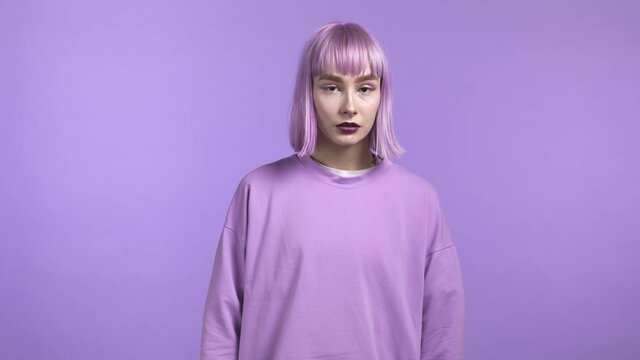 Portrait of millenial trendy woman with dyed violet hair on purple studio background. Serious young girl looking to camera. Amazing make-up and total pastel outfit