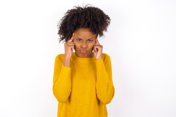 Serious concentrated young beautiful African American woman wearing yellow sweater keeps fingers on temples, tries to ease tension, gather with thoughts and remember important information for exam