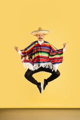 Young man in sombrero and bright poncho isolated over yellow background