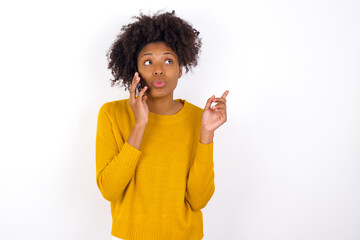 young beautiful African American woman wearing yellow sweater against white wall speaks on mobile phone spends free time indoors calls to friend.