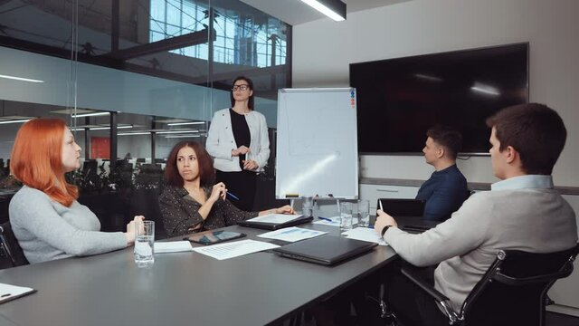 Board of directors having business meeting in office. Female manager reporting on financial success by flipchart with growth graph, multiethnic colleagues discussing and planning strategy