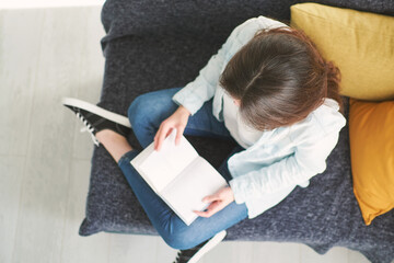 young beautiful woman sitting on a sofa at home and reading a book