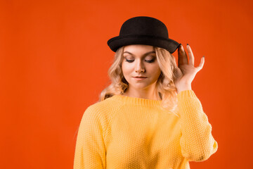 Stylish young woman in knitted clothes and bowler hat, bright orange background