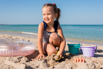 Child girl playing with sand at the beach in summer day. Kids building sand sculptures with shovels and buckets on coast sea. Fun family vacation concept
