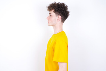young caucasian handsome man with curly hair wearing yellow T-shirt against white studio background  looking to side, relax profile pose with natural face with confident smile.