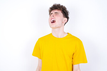 young caucasian handsome man with curly hair wearing yellow T-shirt against white studio background angry and mad screaming frustrated and furious, shouting with anger. Rage and aggressive concept.