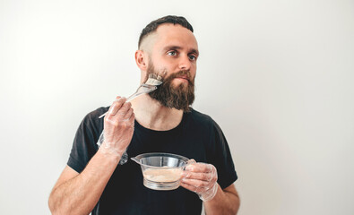 The charismatic guy hipster dyes his beard and hair on white background. Professional beard...