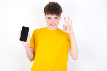 young caucasian handsome man with curly hair wearing yellow T-shirt against white studio background...