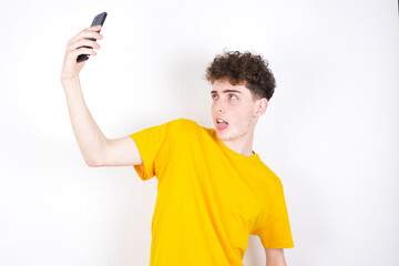 young caucasian handsome man with curly hair wearing yellow T-shirt against white studio background...