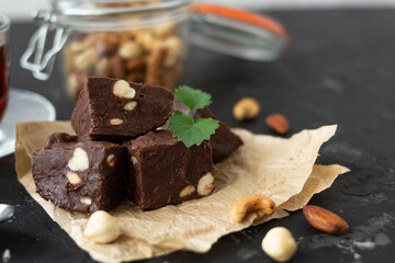 Homemade chocolate fudge garnished with mint leaves and served with tea on a black background. Nuts in the background blurred background. Copy space.