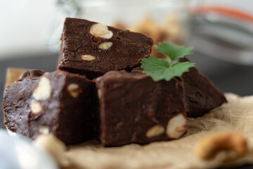 Homemade chocolate fudge garnished with mint leaves and served with tea on a black background. Nuts in the background blurred background. Copy space.