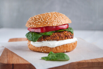 Vegan burger made with red beans, red pepper, spinach, white yoghurt and fresh salad leaves and cut vegetables at the background.