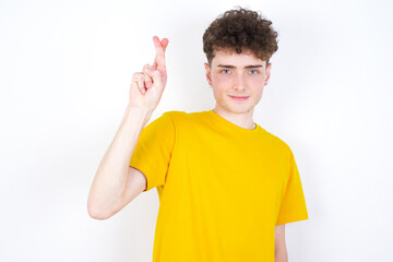 young caucasian handsome man with curly hair wearing yellow T-shirt against white studio background  pointing up with fingers number ten in Chinese sign language Shi