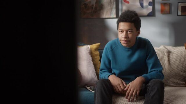 Black Man Teenager Turning On TV And Sitting On Sofa Near Basketball Ball, Eating Popcorn, Young Teen Athlete, Sport Portrait At Home, High School Kid Preparing For Watching Professional Game.