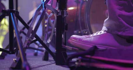 Close-up of the legs of a drummer in sneakers on stage. The drummer kicks the bass drum pedal. Musical group at backgound, live concert. Slow motion - Powered by Adobe