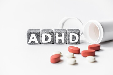 word ADHD is made of stone cubes on a white background with pills. medical concept of treatment, prevention and side effects. attention deficit hyperactivity disorder