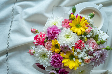 Bouquet of colorful flowers with a white cup on a white tablecloth