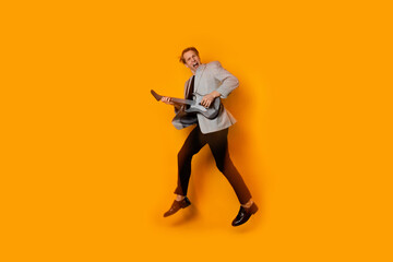 Fototapeta na wymiar Stylish and cool guy in a suit and with a game guitar on a yellow background, playing and dancing,
