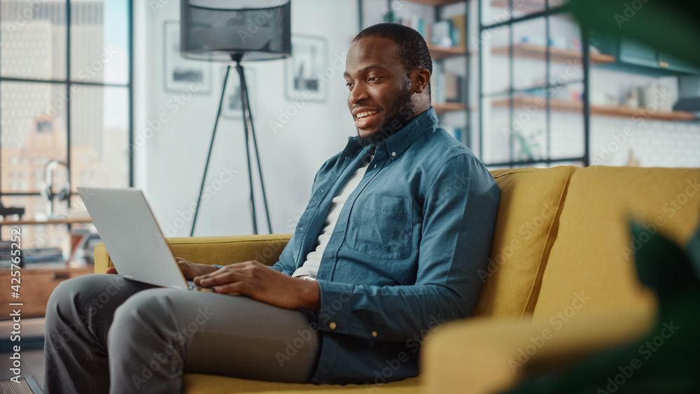 Poster handsome black african american man having a video call on laptop computer while sitting on a sofa i