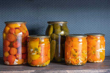Homemade canned summer vegetable pickles: cucumbers, tomatoes, peppers: traditionally canned with herbs and spices. Wooden shelf with homemade products.