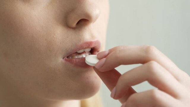 close up of a woman taking a white pill and drinking water.
