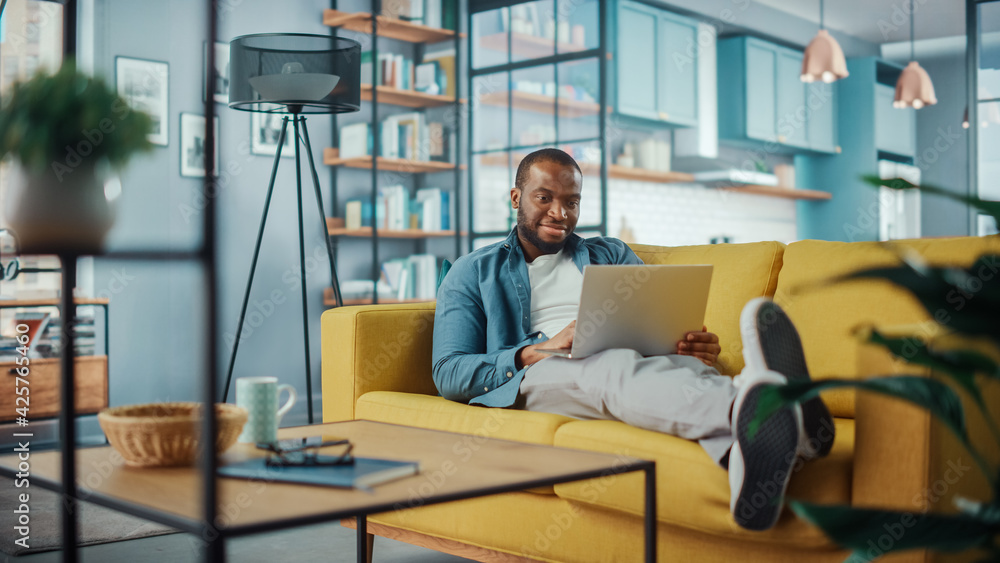 Aufkleber handsome black african american man working on laptop computer while lying on a sofa in cozy living 