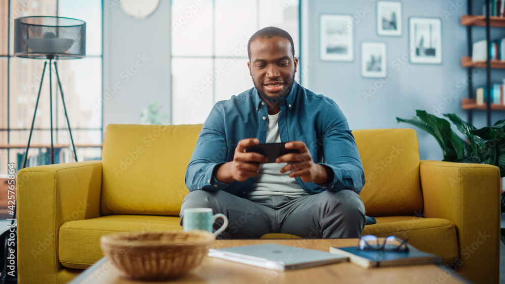 Poster happy black african american man having a playing video game on smartphone app while sitting on a so