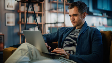 Handsome Caucasian Man Working on Laptop Computer while Sitting on a Sofa in Stylish Cozy Living...