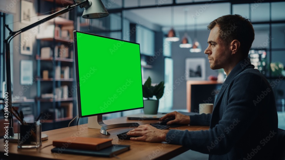 Poster handsome caucasian specialist working on desktop computer with green screen mock up display at home 