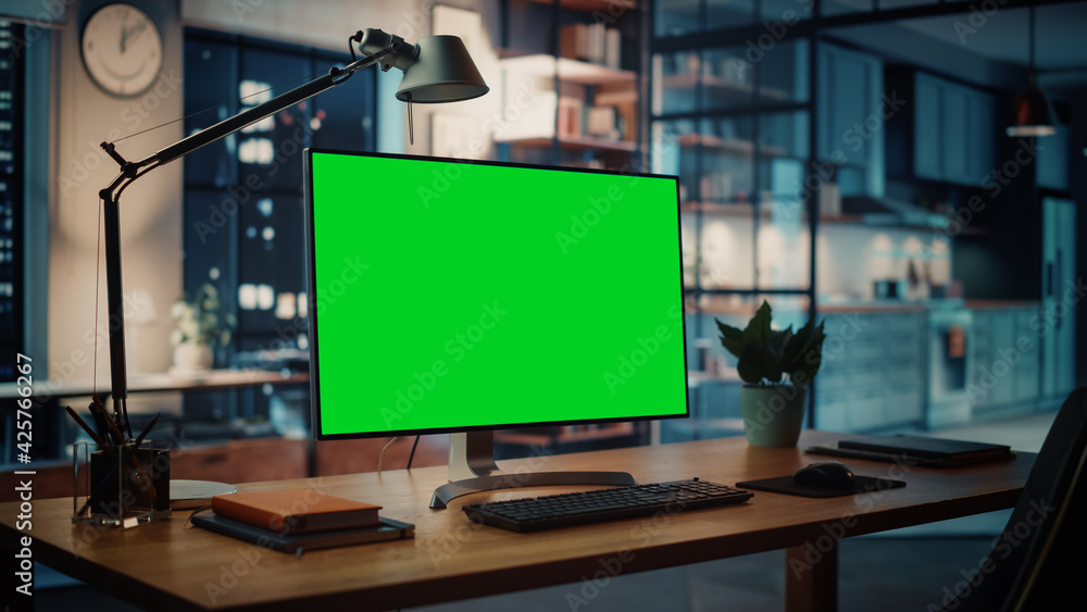 Poster Desktop Computer with Mock-up Green Screen Dsiplay Standing on the Wooden Desk in the Creative Cozy Living Room. In the Background Warm Evening Lighting and Open Space Studio.