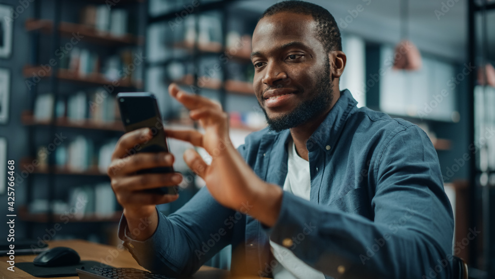 Poster excited black african american man using smartphone while sitting at table in living room. happy man