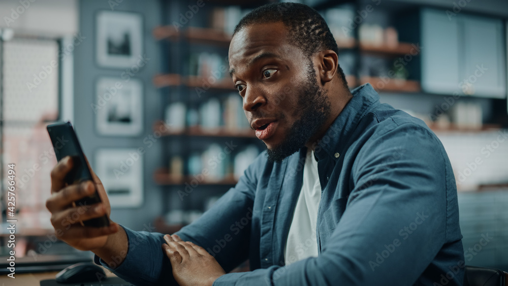 Poster excited black african american man using smartphone while sitting at table in living room. happy man