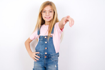 beautiful caucasian little girl wearing denim jeans overall over white background pointing at camera with a satisfied, confident, friendly smile, choosing you