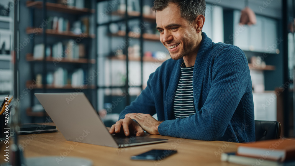 Poster Handsome Caucasian Man Working on Laptop Computer while Sitting Behind Desk in Cozy Living Room. Freelancer Working From Home. Browsing Internet, Using Social Networks, Having Fun in Flat.